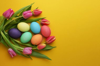 Fresh colorful tulip flowers and easter eggs on yellow background. Top view with copy space. Happy easter greeting card.