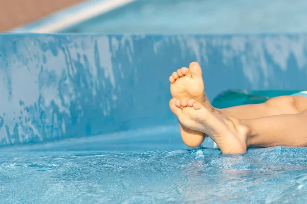 Güneşli bir yaz gününde, mavi havuzda, çıplak ayaklı bir çocuğun ayağını kapat. Mutlu küçük çocuk yüzme havuzunun kenarında oturuyor. Dışarıda yaşam tarzı, mutlu aile yazları..