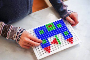 Yaratıcı beyinler oyunda, çocuk çivi mozaiği yapıyor. Konsantre ve titiz, iyi motor beceriler geliştiriyor, şablon tanıma. Basit eğitim oyuncaklarında çocukluk hüneri ve neşesinin kutlanması.