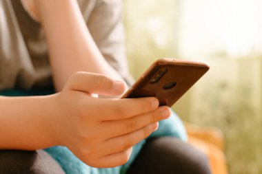 Akıllı telefon tutan ellerin yakın çekimi, Smartphone 'da mesaj gönderen kişi, sıcak doğal ışık altında bulanık bir arka plan. Günlük hayatta mobil teknoloji. Sosyal medya etkileşimi.