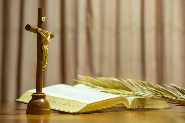 Holy Week religious composition with wooden crucifixion, palm leaf, willow branch, wheat ear. Bible and rosary. Holy week concept, Sunday in copy space.