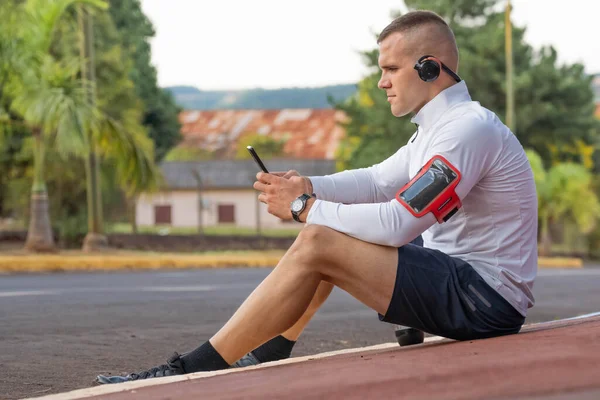 Young male person training, monitoring times with smartphone.