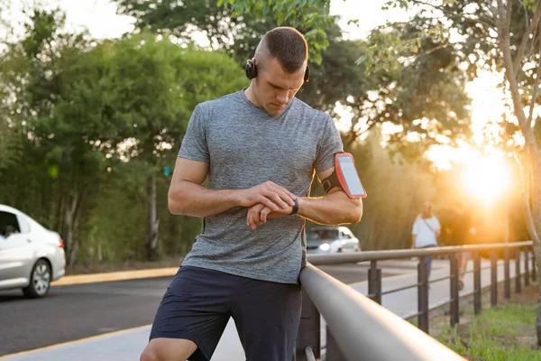 Young male person training, monitoring times with smartphone.