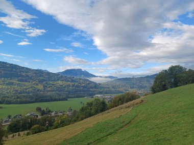 Haute-Savoie, Fransa 'daki Giffre Vadisi' nin manzarası. Yuvarlanan yeşil tarlalar dağlarla çevrili sisli bir vadiye iniyor. Dağılmış bulutlar yumuşak güneş ışığını süzüyor. Doğa, seyahat ve Alp manzarası temaları için ideal