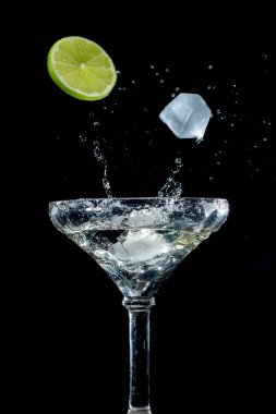 Cocktail in a cocktail glass on a black background with slice of lime and ice cubes