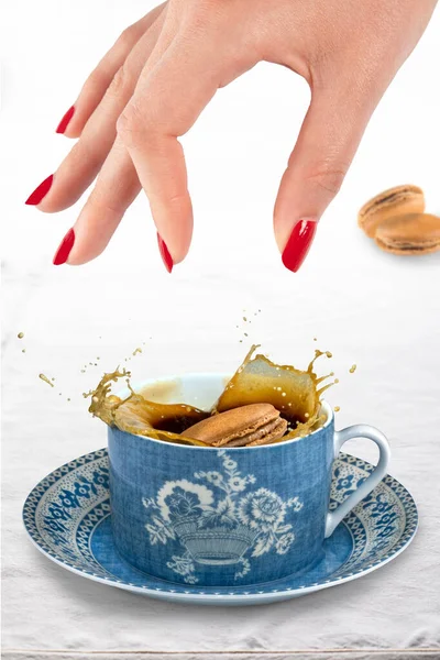 Coffee macaroon being dropped into a cup of coffee from a manicured hand