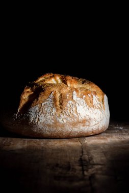 Boule or rustic loaf of french bread on an old wooden table on a black background