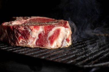 A beef chop cooking on a barbeque with smoke, on a dark background