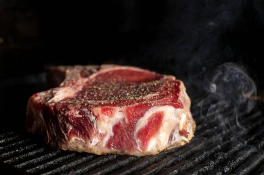 A beef chop cooking on a barbeque with smoke, on a dark background