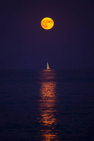 Harvest moon rising over a sailing boat in the Mediterranean sea.