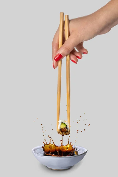 Female hand with red nail varnish and chopsticks splashing sushi into a bowl of soya sauce.