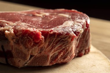 Tahta kesme tahtasındaki çiğ sığır pirzolası şişmanlığı ve mermeri gösteriyor..