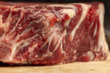 Tahta kesme tahtasındaki çiğ sığır pirzolası şişmanlığı ve mermeri gösteriyor..