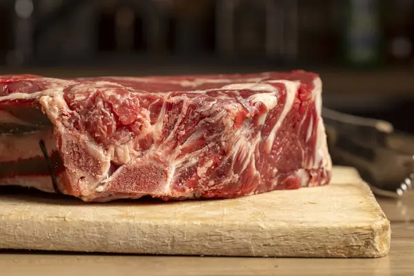 Tahta kesme tahtasındaki çiğ sığır pirzolası şişmanlığı ve mermeri gösteriyor..