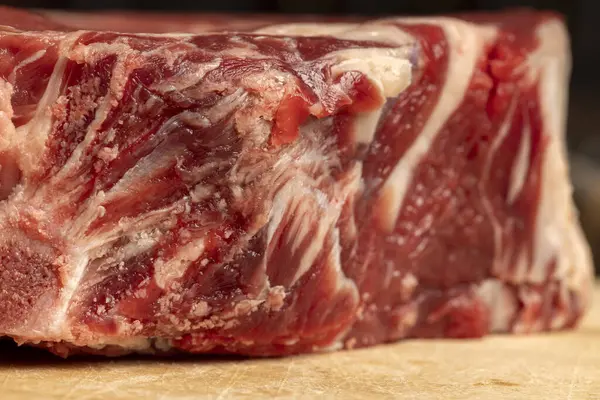 Tahta kesme tahtasındaki çiğ sığır pirzolası şişmanlığı ve mermeri gösteriyor..