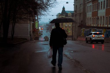 Bir adam elinde fenerle cadde boyunca yürüyor.