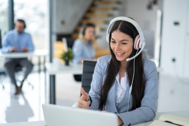 Smiling female helpdesk operator showing thumb up to client during online video call after solving successfully problem at call center.
