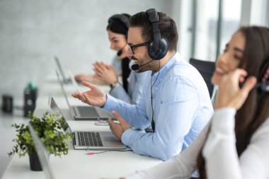 Side view portrait of handsome male IT support executive agent talking to customer while working in call center.