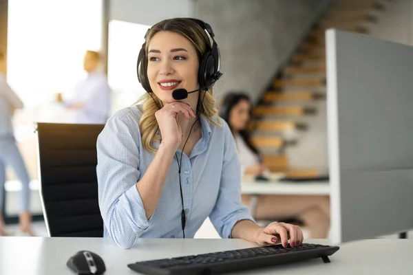 Beautiful female assistant with headset working online with on computer at office
