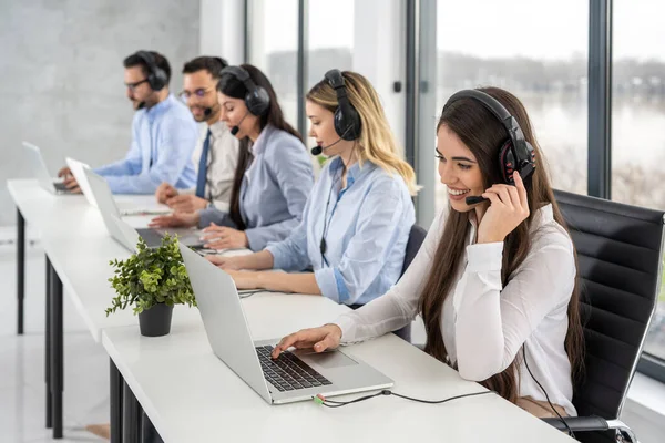 Group of friendly professional customer support operators interacting with clients while having online chats at call center office.