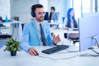 Takım elbiseli başarılı bir işadamı. Etrafı teknoloji ve ofisteki diğer ajanlarla çevrili.