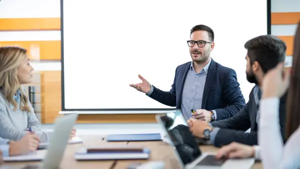 Ofisteki iş ortaklarının önünde beyaz yönetim kurulunda sunum yapan kendine güvenen bir iş adamı. Boşluğu beyaz tahtada kopyala.