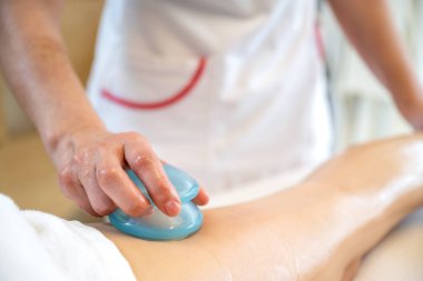 Mantar şekilli Gua Sha şeklindeki selülit önleyici alet ve güzellik salonundaki müşterilerin bacağına masaj yapmak..