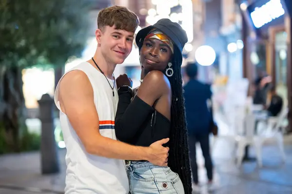 Portrait of happy young mixed couple in love posing together on the city street at night