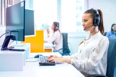 Kulaklık takan IT servis operatörü kadın çağrı merkezinde bilgisayar üzerinde çalışıyor..
