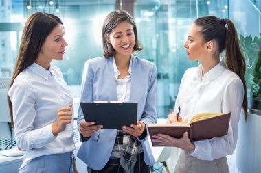 Not defterleri ve kağıt klasörleri olan üç kendine güvenen iş kadını güzel mavi modern ofiste kurumsal açıklamalardan bahsediyorlar..