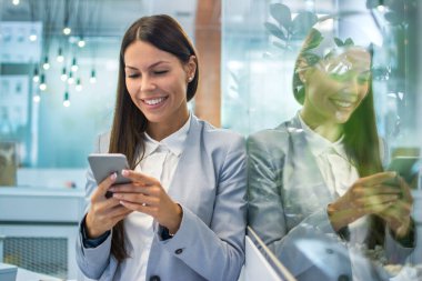 Ofiste kısa bir aradan sonra yansıması ve kayan sosyal medya ağlarıyla cama yaslanan gülümseyen iş kadını.