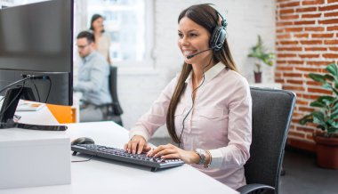 Modern bir ofiste kulaklık ve bilgisayar kullanan genç bir kadının portresi..