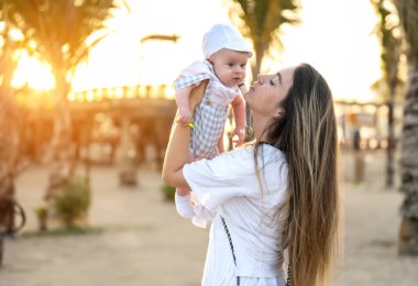 Annenin gün batımında bebeğine sarılışının yan görüntüsü. Genç bir anne ve güzel çocuğu arasındaki bağ ve birliktelik kavramı..