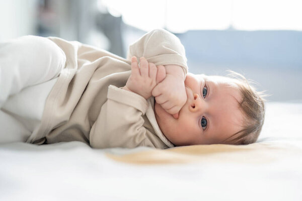 Портрет мальчика, лежащего на кровати с руками во рту.