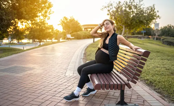 木製のベンチに休んで 公園で美しい夕日を楽しんでいる若い妊婦 — ストック写真