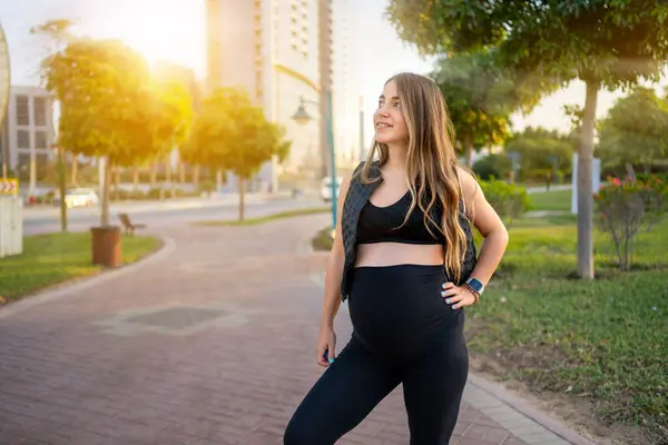 公園の歩道に立って 日没の間に離れて見ているかなり妊娠した女性 — ストック写真