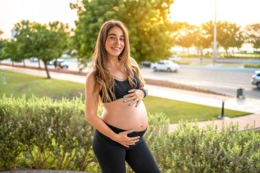 Dışarıda karnına dokunan çekici hamile bir kadının portresi. Hamilelik, bebek beklemek, sağlıklı yaşam tarzı konsepti.