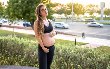 Çekici hamile kadın dışarıda karnına dokunuyor. Hamilelik, bebek beklemek, sağlıklı yaşam tarzı konsepti.