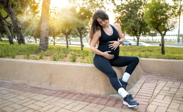 Zwangere Vrouw Sportkleding Zit Stenen Muur Raakt Haar Buik Buiten — Stockfoto