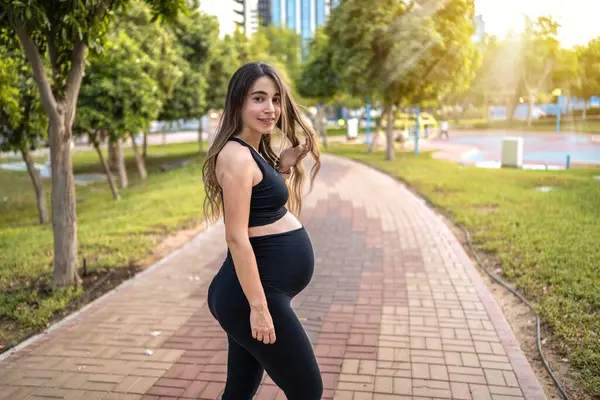 彼女の髪を保持し 公園の歩道に立っているスポーツウェアで9ヶ月の妊婦の肖像画 — ストック写真