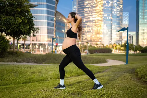 夜に公園で肺をやっているスポーツウェアの妊婦の側面のビュー — ストック写真
