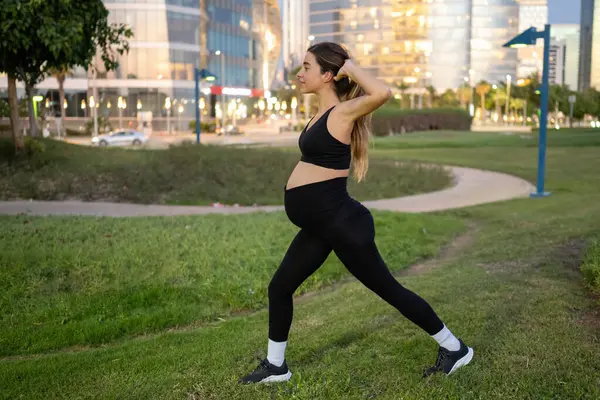 夜に公園で肺や運動をしているスポーティな服の妊婦の側面ビュー — ストック写真