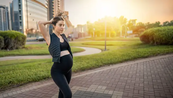 若い妊婦が日没で公園を散歩しながら髪を結ぶ — ストック写真