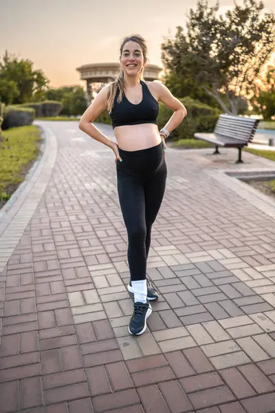 日没の公園に立っているスポーツウェアの美しい若い妊婦 — ストック写真