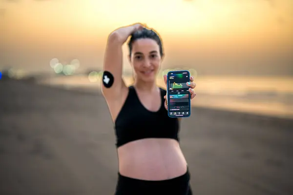 糖尿病制御を改善するために連続的なグルコースモニターを使用して美しい妊婦 スマートフォンアプリで血糖検査を表示する携帯電話を示すスポーティな妊婦 — ストック写真