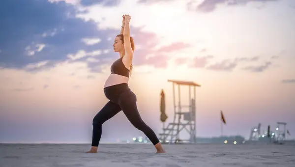 日落时分 身穿黑色运动服的孕妇在海滩上摆出全长侧面肖像 使新月隆起瑜伽成为一种姿势 瑜伽和怀孕的概念 — 图库照片