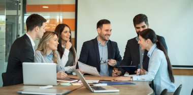 Bir grup genç iş adamı konferans odasında ofis masasında birlikte otururken çalışıyor ve iletişim kuruyor.