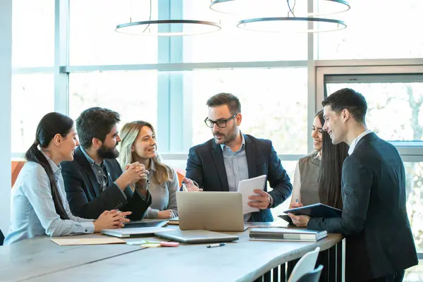 İş adamları toplantı masasında oturmuş laptopta iş ve planlama stratejilerini tartışıyorlar.