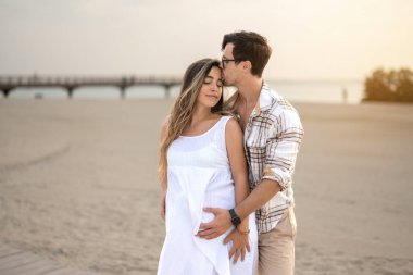 Yakışıklı bir adam gün batımında hamile karısını öpüyor ve ona sarılıyor.