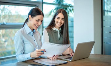 Gülümseyen iş arkadaşları ofiste kağıt dökümanlarını tartışıyorlar.